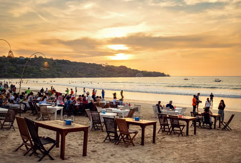 Wide-angle view of Jimbaran Beach at sunset with tables set up for seafood dining along the shoreline